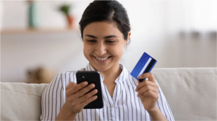 Woman smiling at phone while holding debit card